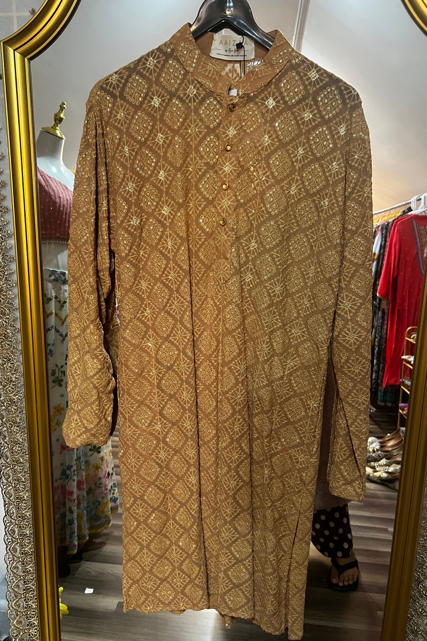 Gold patterned garment on a hanger in front of a mirror