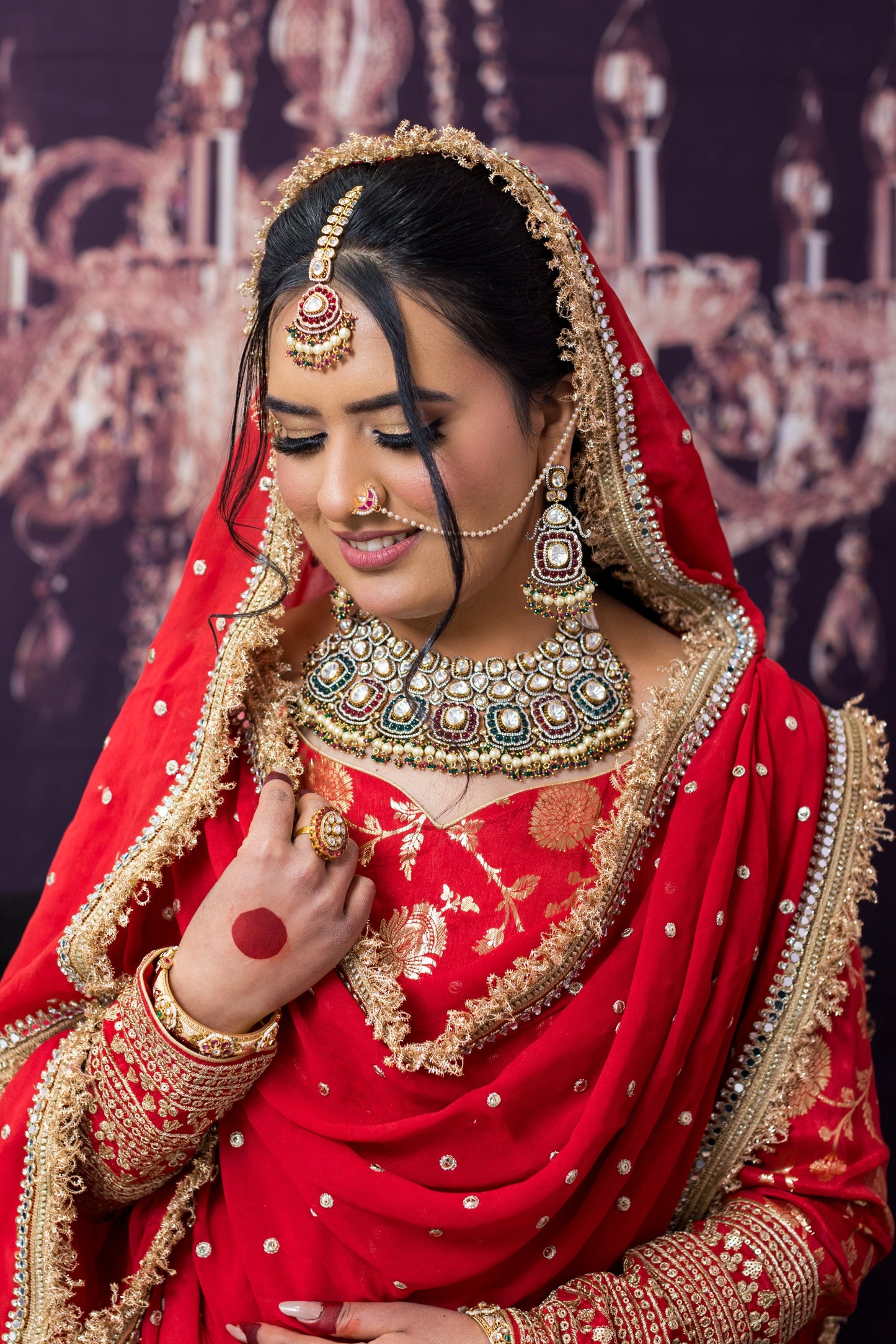 Woman in traditional red bridal outfit with gold jewelry against a decorative backdrop