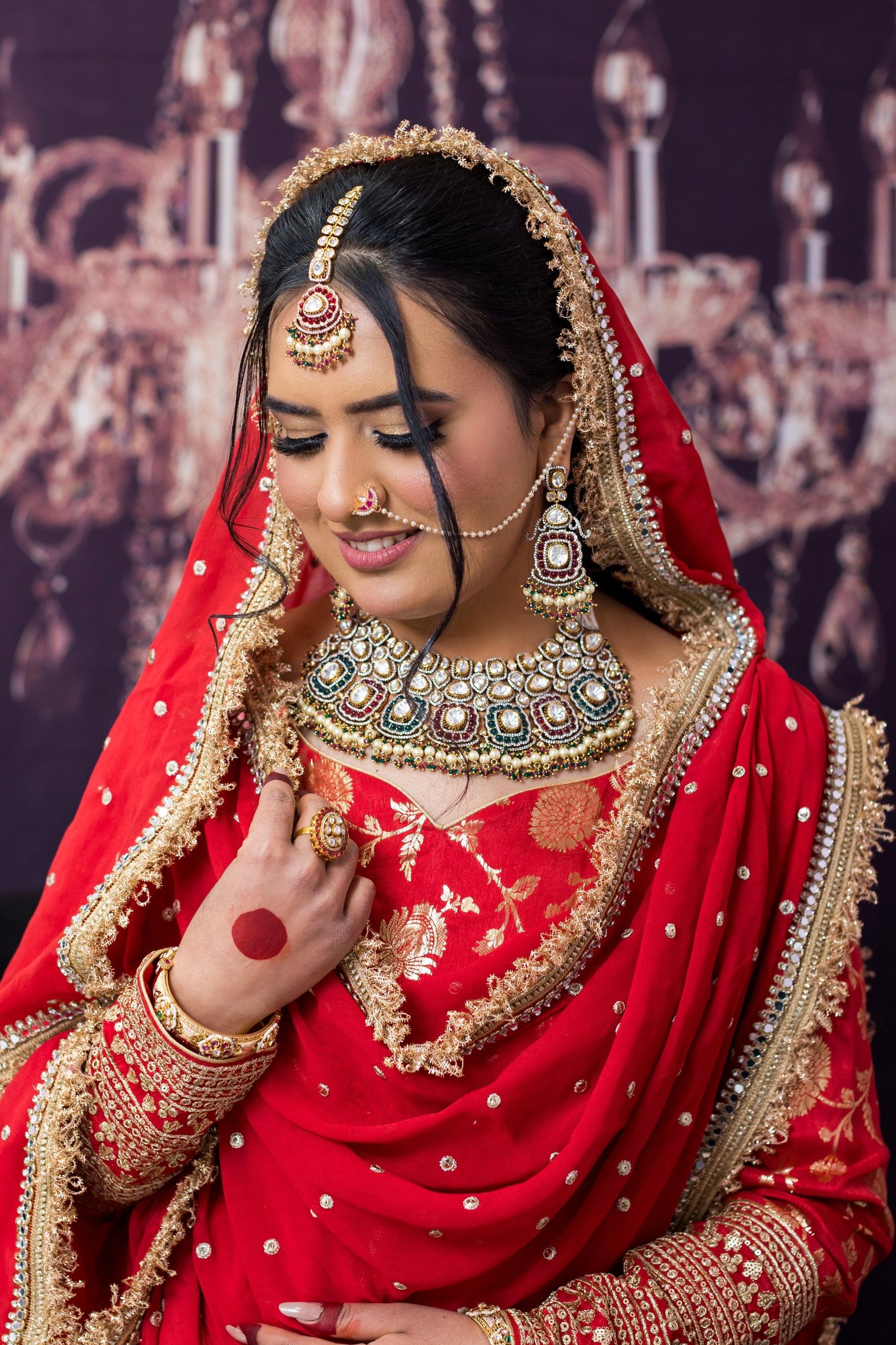 Woman in traditional red bridal outfit with gold jewelry against a decorative backdrop