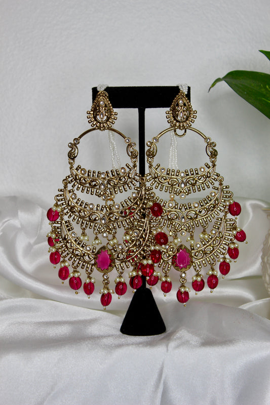 Ornate earrings with red beads on a black stand against a white background