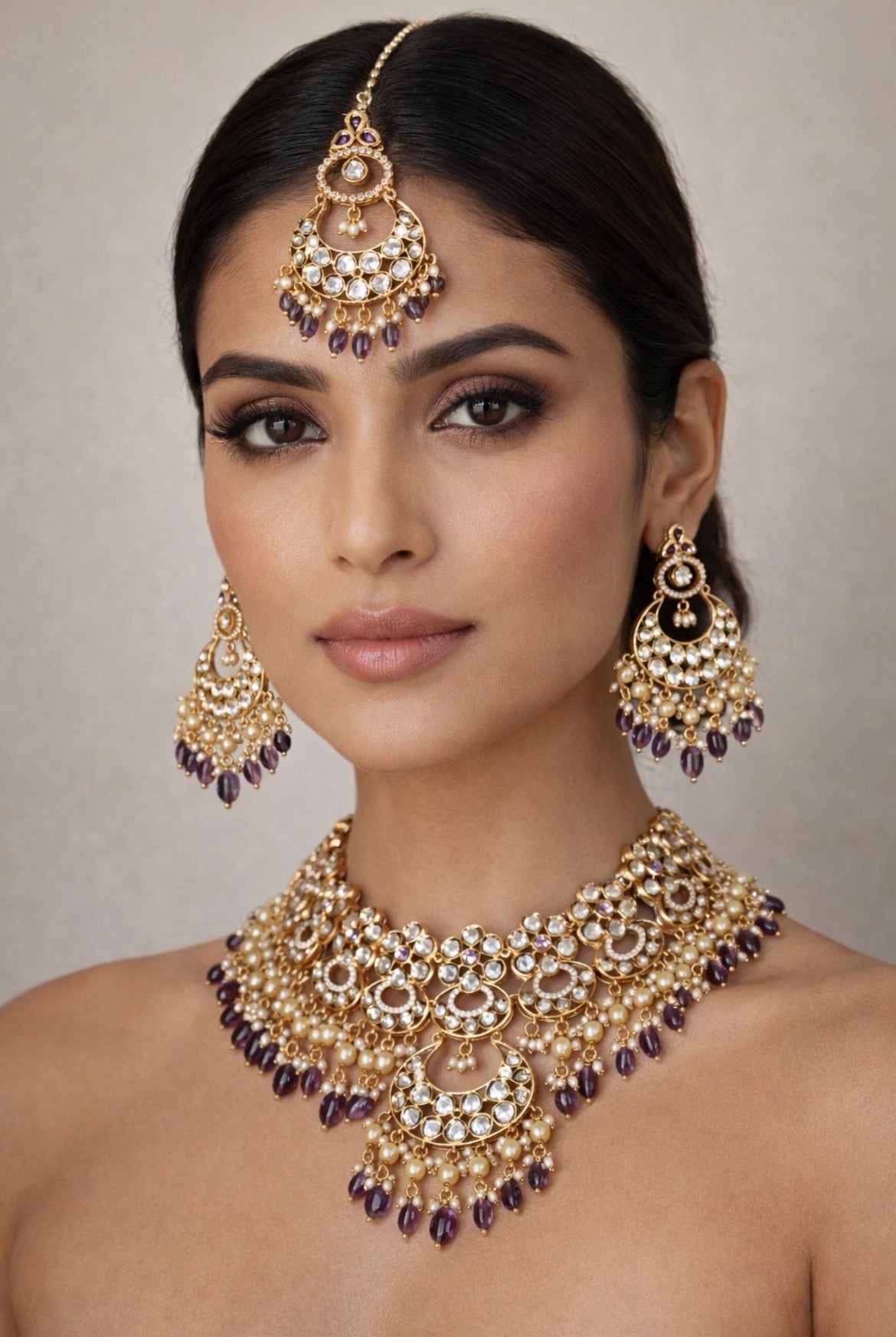 Woman wearing an elaborate gold and purple jewelry set against a neutral background